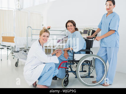 Vista laterale dei medici con paziente di sesso femminile in sedia a rotelle in ospedale Foto Stock
