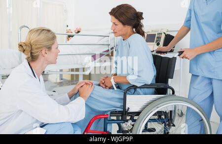 Vista laterale di un medico parlando a un paziente di sesso femminile in sedia a rotelle in ospedale Foto Stock