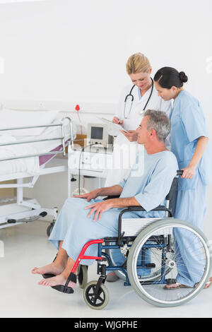 Vista laterale di un medico parlando a un paziente di sesso maschile in sedia a rotelle in ospedale Foto Stock