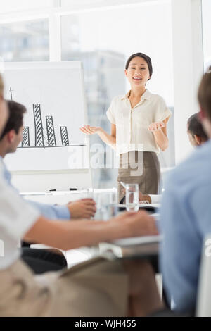 Felice asian imprenditrice presentando grafico a barre a co lavoratori in ufficio Foto Stock