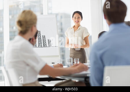 Felice asian imprenditrice presentando grafico a barre a colleghi in ufficio Foto Stock