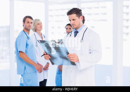 Concentrato medico maschio esaminando x-ray con i colleghi in piedi dietro a un ufficio medico Foto Stock