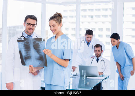 Sorridente medici esaminando x-ray con i colleghi utilizzando il laptop in un ufficio medico Foto Stock