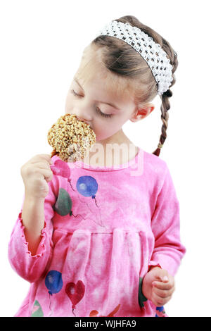 Adorabile bambina mangia una mela caramellata contro uno sfondo bianco. Foto Stock