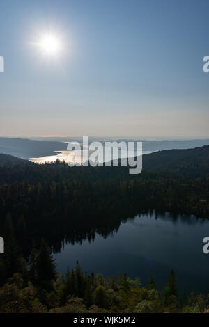 Ritratto del tramonto sopra i fiordi al di fuori di Bergen, Norvegia in background e con alberi riflessa in vetro-come il lago in primo piano. Foto Stock