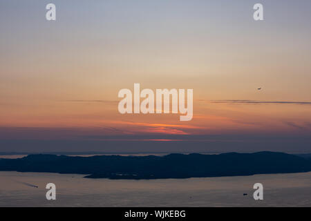 Tramonto su i fiordi al di fuori di Bergen, Norvegia, con un aeroplano che vola verso il tramonto e due barche che attraversa il fiordo. Foto Stock