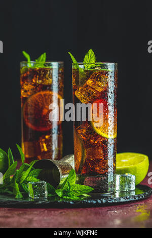 Il freddo Longdrink Cuba Libre marrone con il rum e lime fresco highball in vetro con gocce di acqua su sfondo scuro, il fuoco selettivo Foto Stock