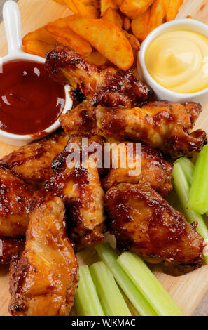 Succose le cosce di pollo e le ali di barbecue con Patatine fritte, ketchup, salsa di formaggio e Sedano closeup sulla tavola di legno. Vista superiore Foto Stock