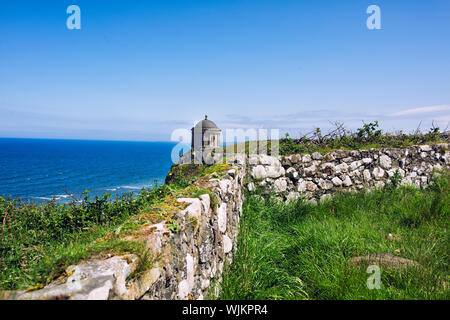 Mussenden Temple contro il cielo blu e l'Oceano Atlantico sulla costa nordoccidentale dell'Irlanda del Nord Foto Stock