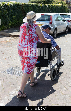 Una donna di mezza età spingendo un uomo anziano in una sedia a rotelle, i vecchi/persona disabile con accompagnatore Foto Stock