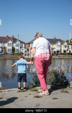 Una nonna si tengono per mano con suo nipote di un piccolo ragazzo di stagno delle anatre Foto Stock