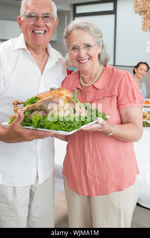 Ritratto di coppia senior tenendo il pollo arrosto in casa Foto Stock