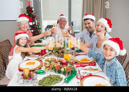 La famiglia felice in cappelli di Babbo Natale tostatura di bicchieri di vino a tavola da pranzo nella casa Foto Stock