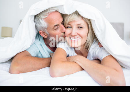 Primo piano di un uomo maturo kissing womans guancia a letto di casa Foto Stock