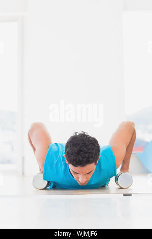 Giovane determinato facendo ups push con manubri in studio fitness Foto Stock