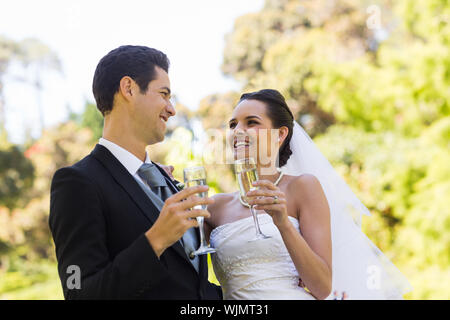 Felice giovane sposa giovane tostatura flauti di champagne presso il parco Foto Stock