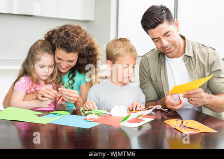La famiglia felice facendo arti e mestieri assieme al tavolo a casa in cucina Foto Stock