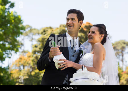 Felice giovane sposa giovane con bottiglia di champagne presso il parco Foto Stock