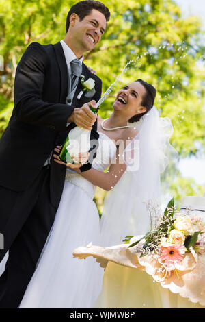 Felice giovane sposa giovane con lo sposo di aprire la bottiglia di champagne al park Foto Stock