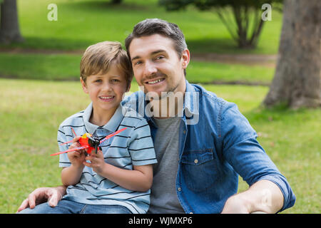 Ritratto di un giovane ragazzo con aeroplano giocattolo seduto sul padre di giro al parco Foto Stock