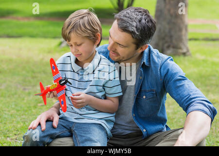 Ragazzo con aeroplano giocattolo seduto sul padre di giro al parco Foto Stock