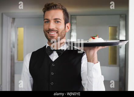 Sorridente cameriere tenendo il vassoio con la piastra di dessert in un ristorante elegante Foto Stock