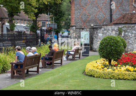 Winchester, Hampshire, Regno Unito la gente seduta sulle panche di legno in un British parco o giardino circondato da fiori e prati tagliati Foto Stock