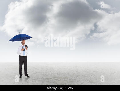 Happy businessman holding ombrello contro sfondo con cielo nuvoloso Foto Stock
