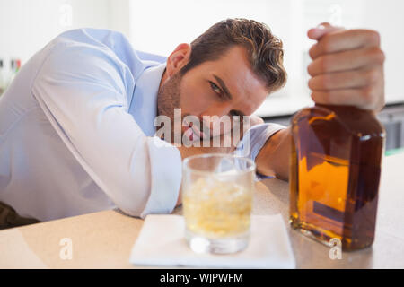 Imprenditore ubriaco che impugnano whiskey bottiglia guardando la fotocamera presso il bar locale Foto Stock