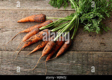 Freschi carote lavate con verdi su vecchie tavole di legno Foto Stock