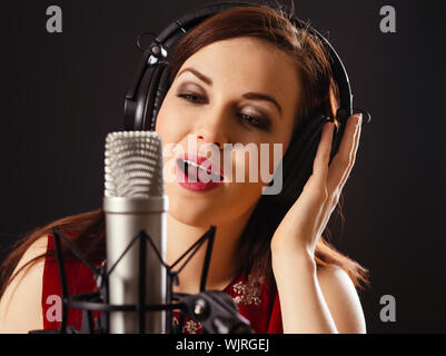 Foto di una bella donna cantare in un diaframma grande microfono su sfondo scuro. Foto Stock