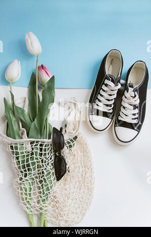 Borsa di stringa con i tulipani, casual sneakers e nero elegante occhiali da sole. Appartamento laico, vista dall'alto il concetto di estate. Il concetto di riciclaggio, co friendly, rifiuti zero. Foto Stock