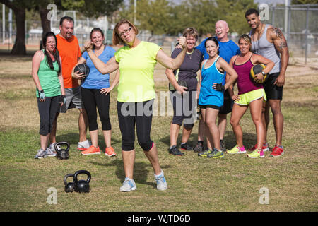 Fiducioso donna matura la flessione delle braccia con gruppo di fitness in piedi Foto Stock