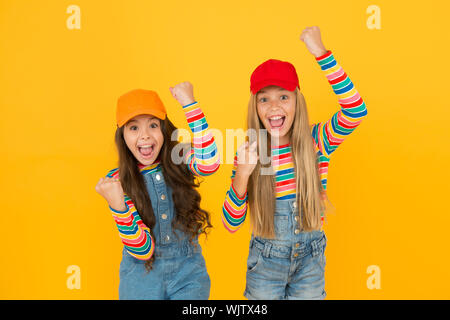 Essere felice e vittoriosa. Bambine compiendo gesti di vittoria su sfondo giallo. Carino piccolo vincitori godendo la vittoria insieme. Dei bambini felici celebrando la vittoria o il successo. La vittoria e il trionfo. Foto Stock