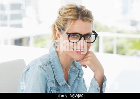 Designer biondo con gli occhiali sorridente in telecamera in ufficio creativo Foto Stock