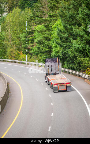 Big Rig professionale potente di grado industriale scuro cabina alta cofano semi carrello vuoto con letto piano semi rimorchio andando al magazzino per i carichi in esecuzione o Foto Stock