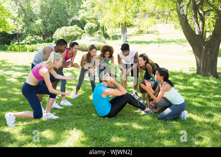 Gruppo di amici tifo uomo facendo sit ups nel parco Foto Stock