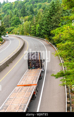 Big Rig professionale potente di grado industriale scuro cabina alta cofano semi carrello vuoto con letto piano semi rimorchio andando al magazzino per i carichi in esecuzione o Foto Stock