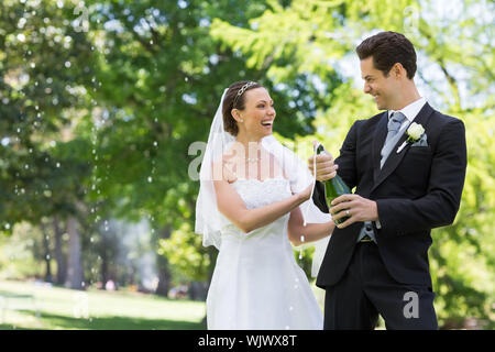 Giovane sposa giovane di apertura della bottiglia di champagne in posizione di parcheggio Foto Stock