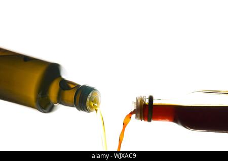 Olio di oliva e aceto versata da bottiglie isolato su bianco Foto Stock