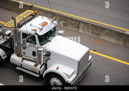 White potente cabina giorno big rig di grado industriale semi carrello con giallo carico oversize segno sul tetto in esecuzione sull'autostrada strada al punto di carico Foto Stock