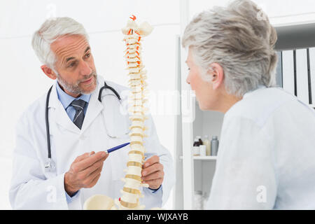 Medico di sesso maschile che spiega la spina dorsale per senior paziente in ufficio medico Foto Stock