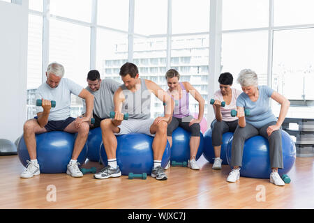 Ritratto della lezione di fitness con manubri seduti su palle ginniche in una luminosa palestra Foto Stock