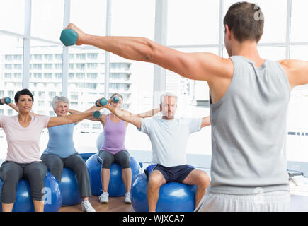 Ritratto della lezione di fitness con manubri seduti su palle ginniche in una luminosa palestra Foto Stock