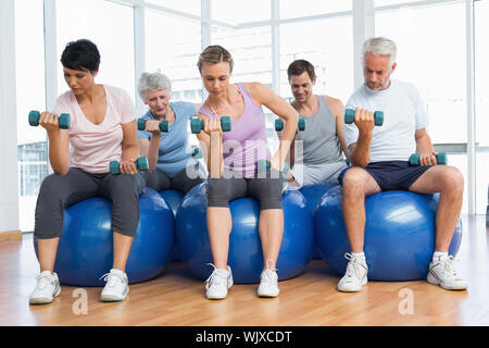 Ritratto della lezione di fitness con manubri seduti su palle ginniche in una luminosa palestra Foto Stock