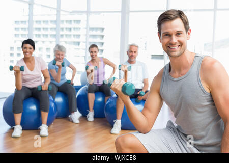 Ritratto della lezione di fitness con manubri seduti su palle ginniche in una luminosa palestra Foto Stock