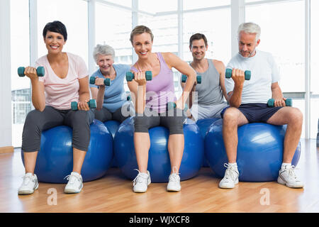 Ritratto della lezione di fitness con manubri seduti su palle ginniche in una luminosa palestra Foto Stock