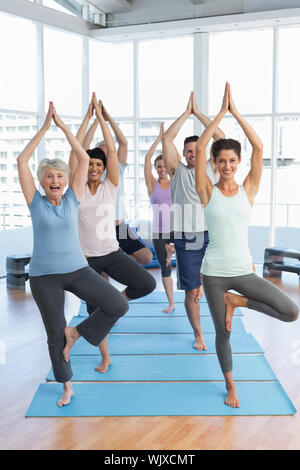 Ritratto di un trainer sorridente con classe in piedi in posizione dell'albero a lezione di yoga Foto Stock