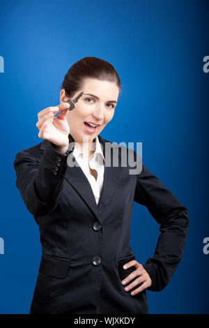 Giovane e bella donna d'affari chiavi olding su uno sfondo blu Foto Stock