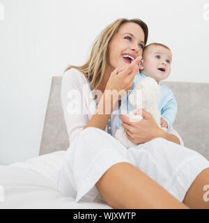 Allegro la madre e il bambino con il giocattolo imbottito che guarda lontano nel letto Foto Stock